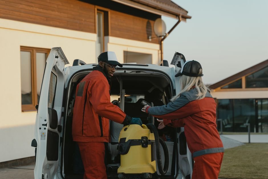 Agents d'entretien en tenue rouge chargeant un aspirateur professionnel dans un utilitaire